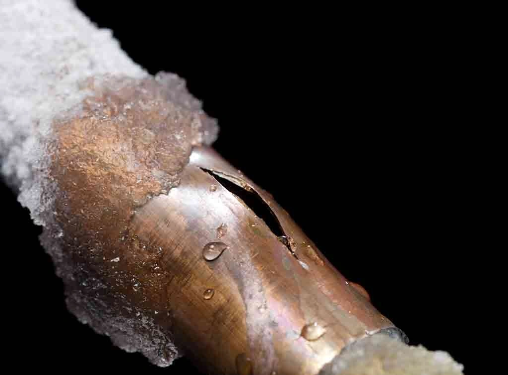 Frozen burst pipe with ice crystals and water droplets against black background
