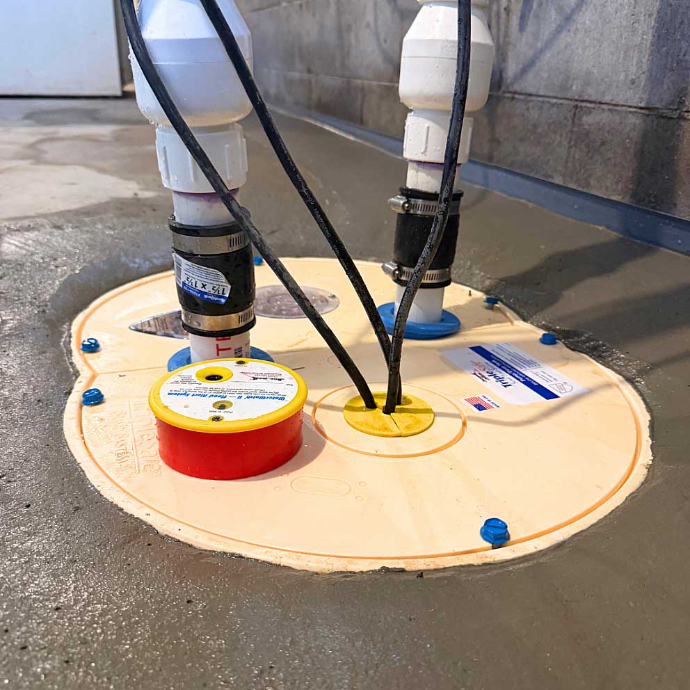 A white sump pump systems with black cords installed in a concrete floor pit, demonstrating basement water management equipment