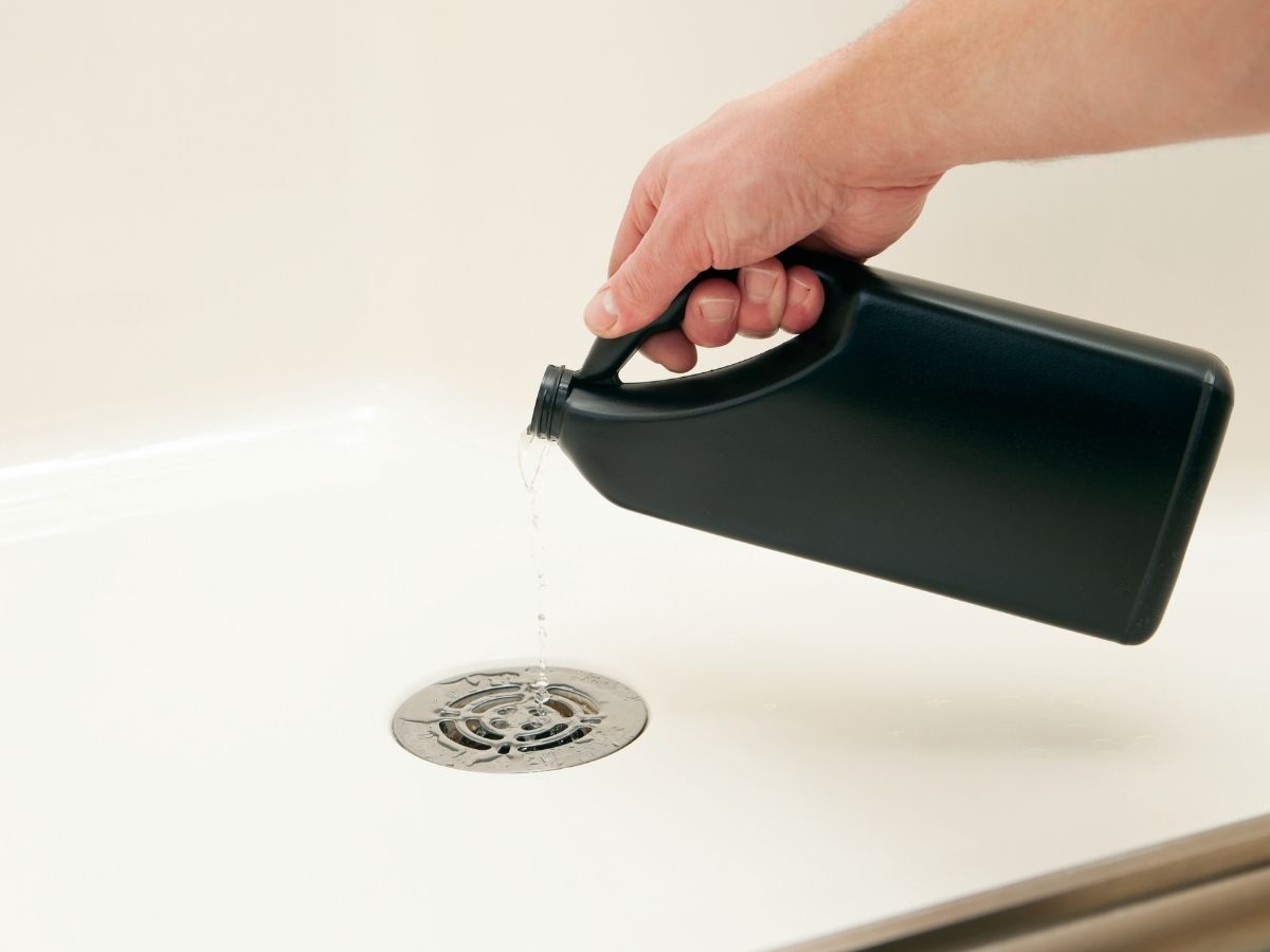 Hand pouring liquid down a ceiling drain vent opening