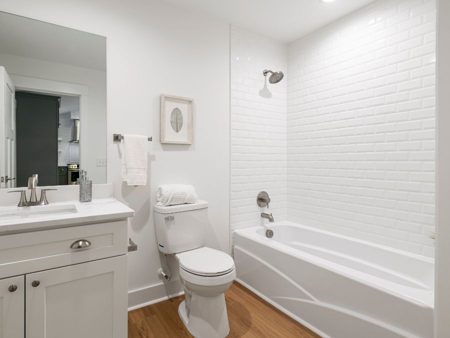 Modern bathroom with white subway tile shower surround, white vanity with sink, toilet, and bathtub with chrome fixtures on wood-look flooring