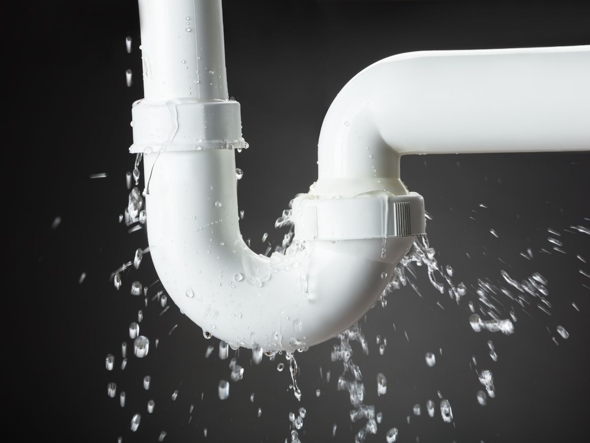 White P-trap plumbing pipe bursting and spraying water against dark background