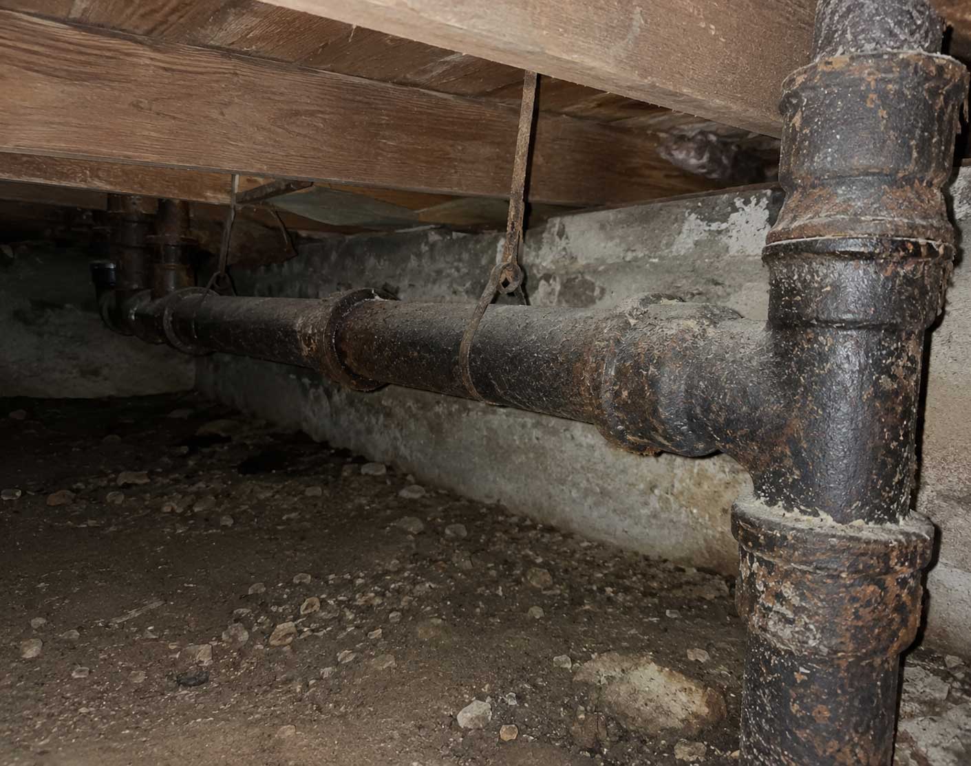 Rusty cast-iron pipe and wooden beam support structure in industrial basement or cellar space