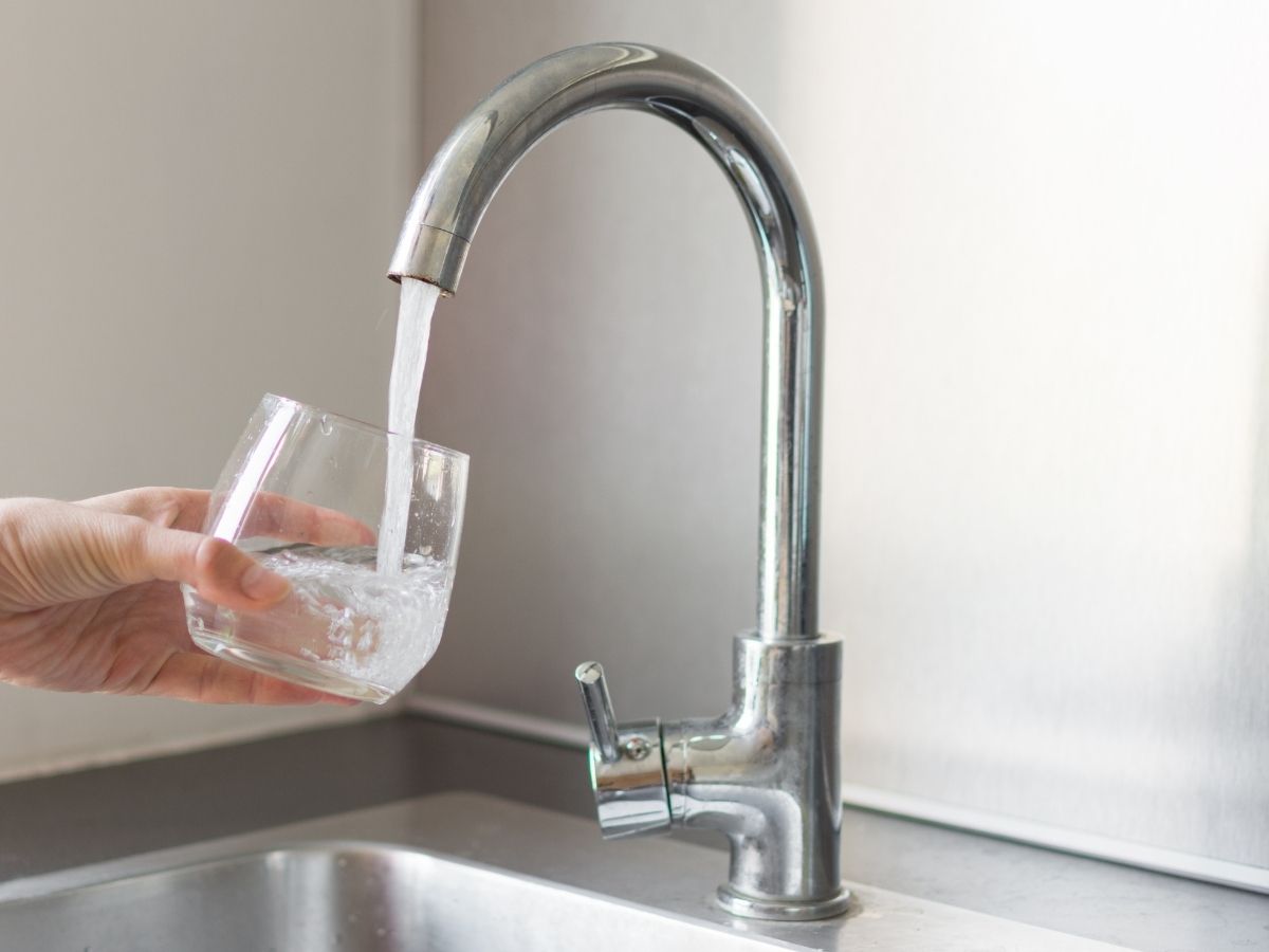 Hand holding glass filling with clean tap water from modern kitchen faucet