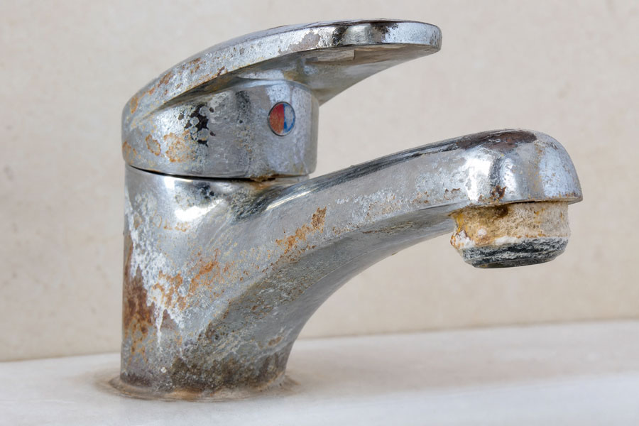 Corroded chrome bathroom faucet with rust stains and patina, showing significant wear and age