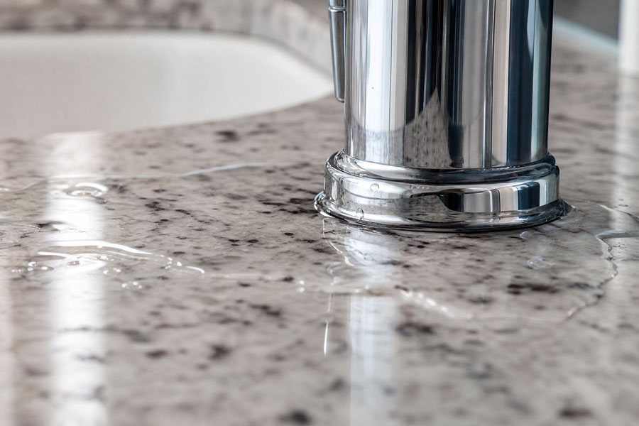 Chrome faucet with water pooling on speckled gray countertop surface