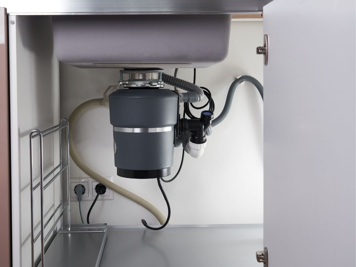 Under-sink garbage disposal unit with motor and drain pipes installed in kitchen cabinet
