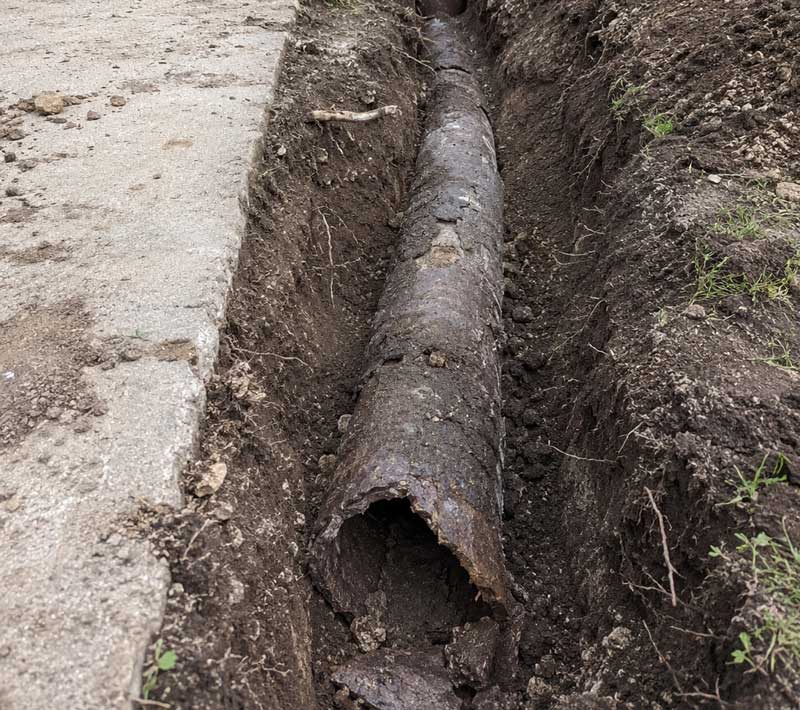 Deteriorated Orangeburg pipe in trench showing corrosion and damage, exposed underground utility line