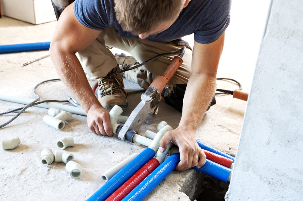 Plumber installing PVC pipes and connectors on a concrete floor during a construction or renovation project