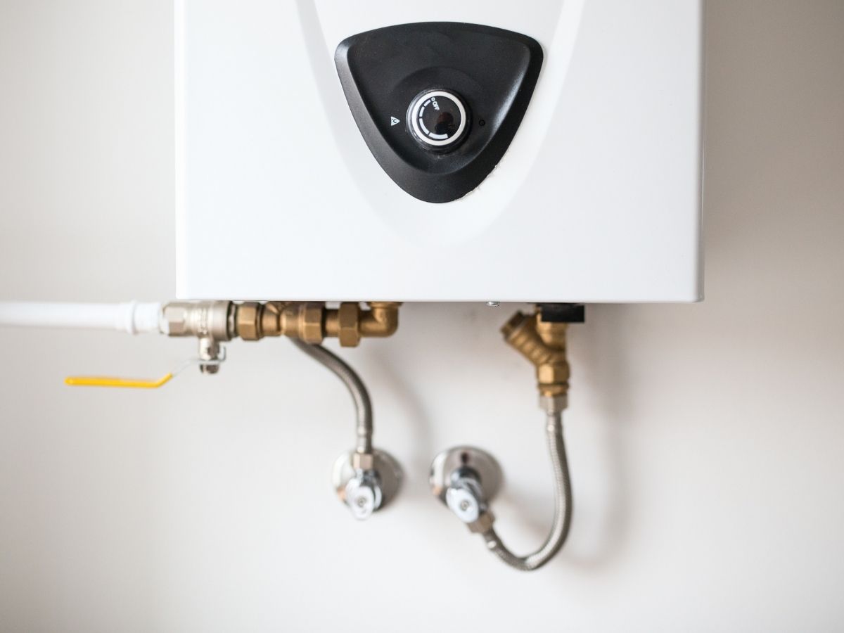 White tankless water heater mounted on wall with brass fittings and shut-off valves below